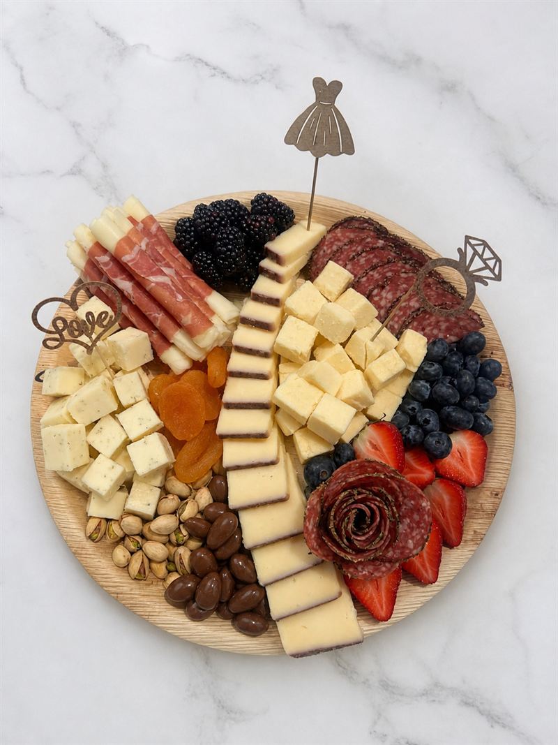 Small charcuterie board topped with wedding dress, engagement ring and Love picks, with a salami rose, cheeses and berries